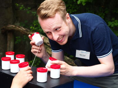 Mitarbeiter Niklas Theiler spielt das Hör-Memory mit einem Kind am Forschertag